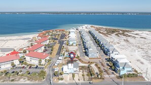 Vista aerea di una località balneare con proprietà sul lungomare, un porto turistico e un cielo azzurro terso.