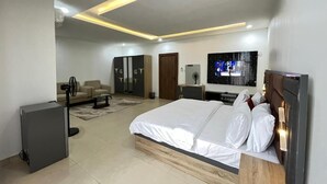 Un dormitorio moderno con una cama grande, un televisor, un escritorio y un ventilador.