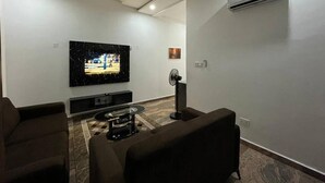 Una sala de estar moderna con un televisor de pantalla plana montado en la pared, un ventilador de pie y un sofá.