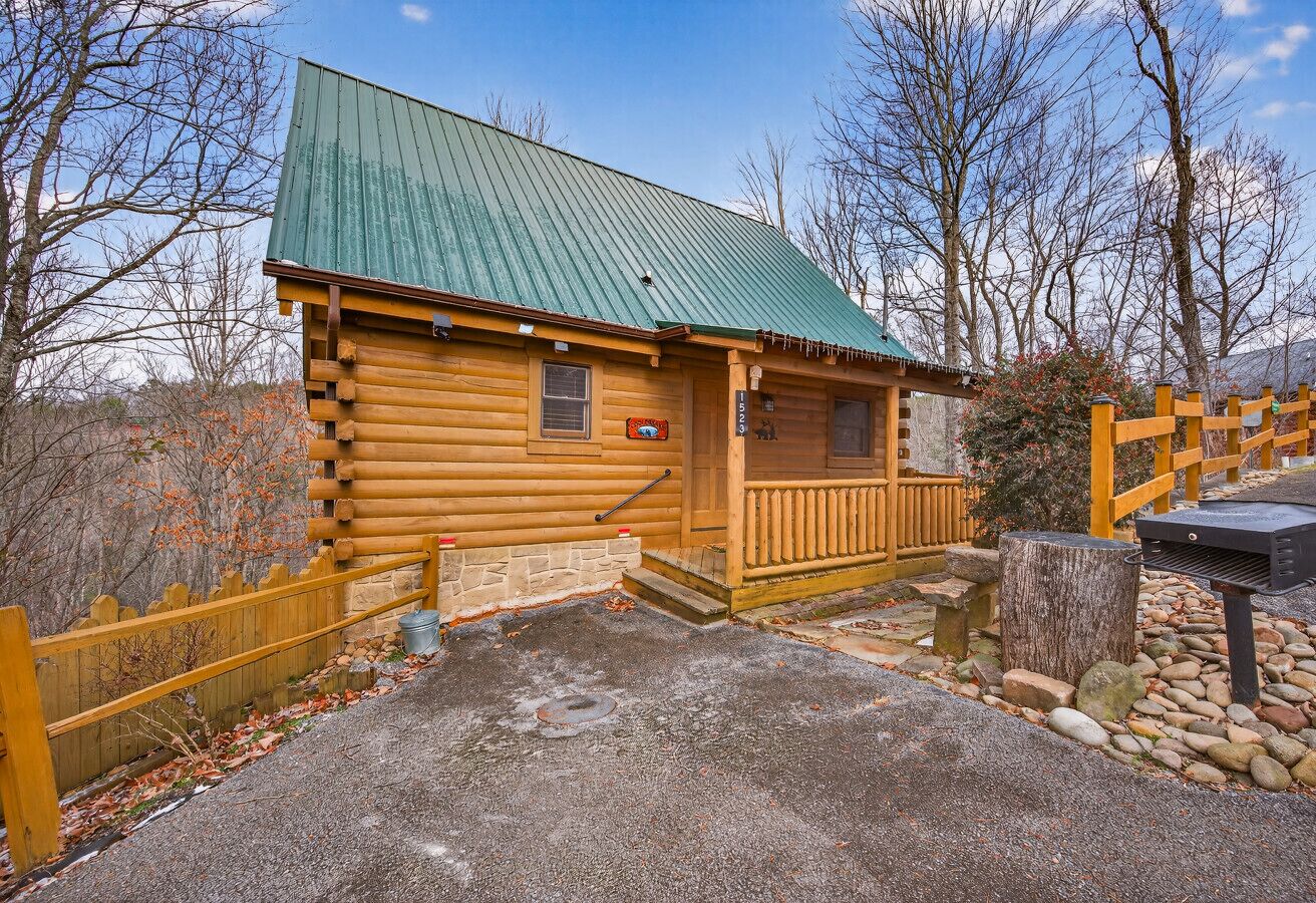 A log cabin with a green roof, wooden porch, and a stone wall.