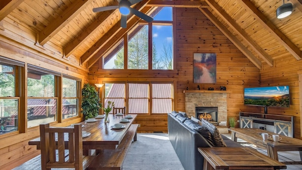 Een chaletinterieur met een eethoek, zitplaatsen, een open haard en een televisie.