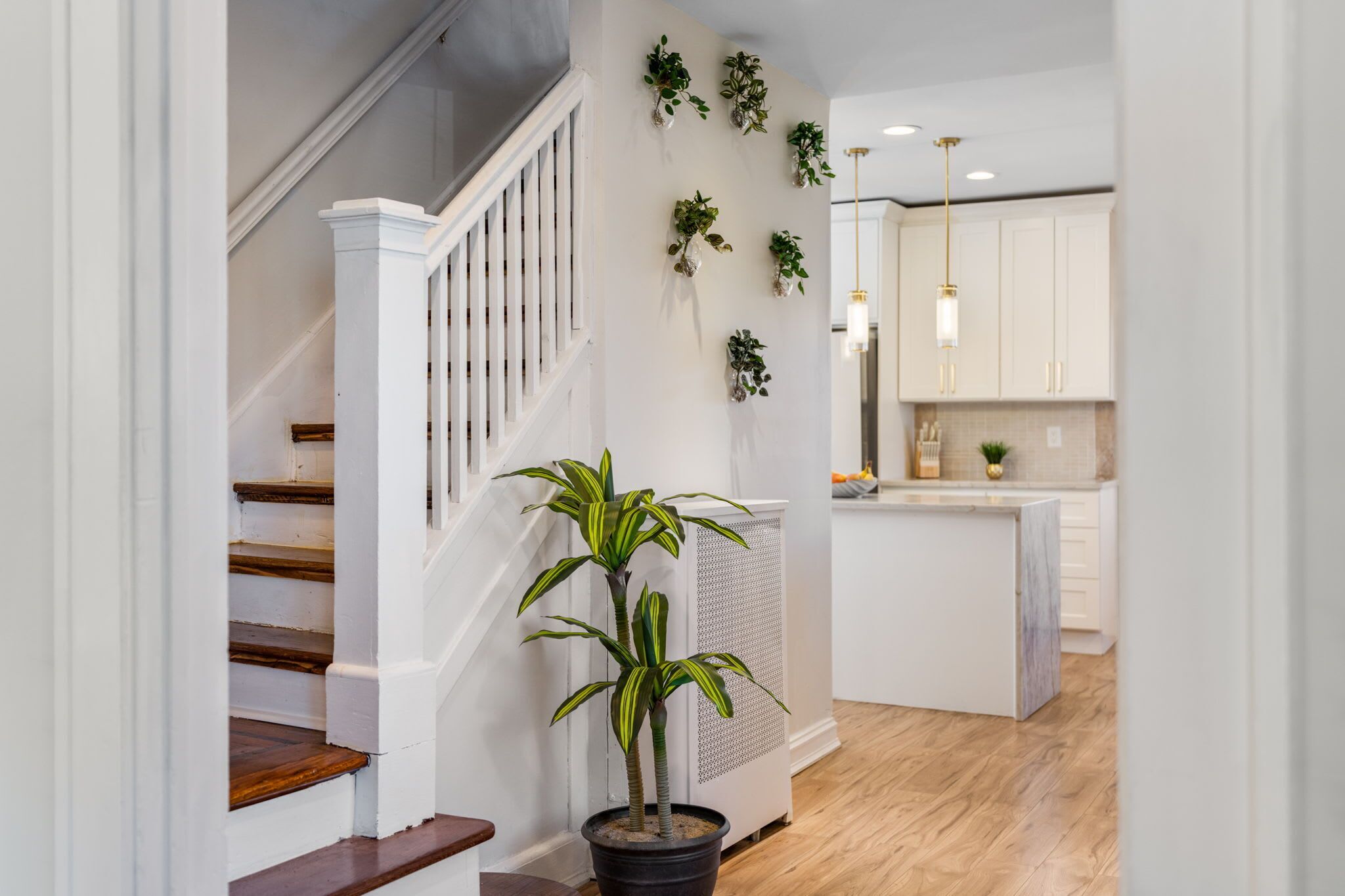 A modern interior with a staircase, potted plants, and a kitchen area.