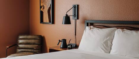 Une chambre d’hôtel avec un lit, une chaise, une table de chevet avec une lampe et un tableau au mur.