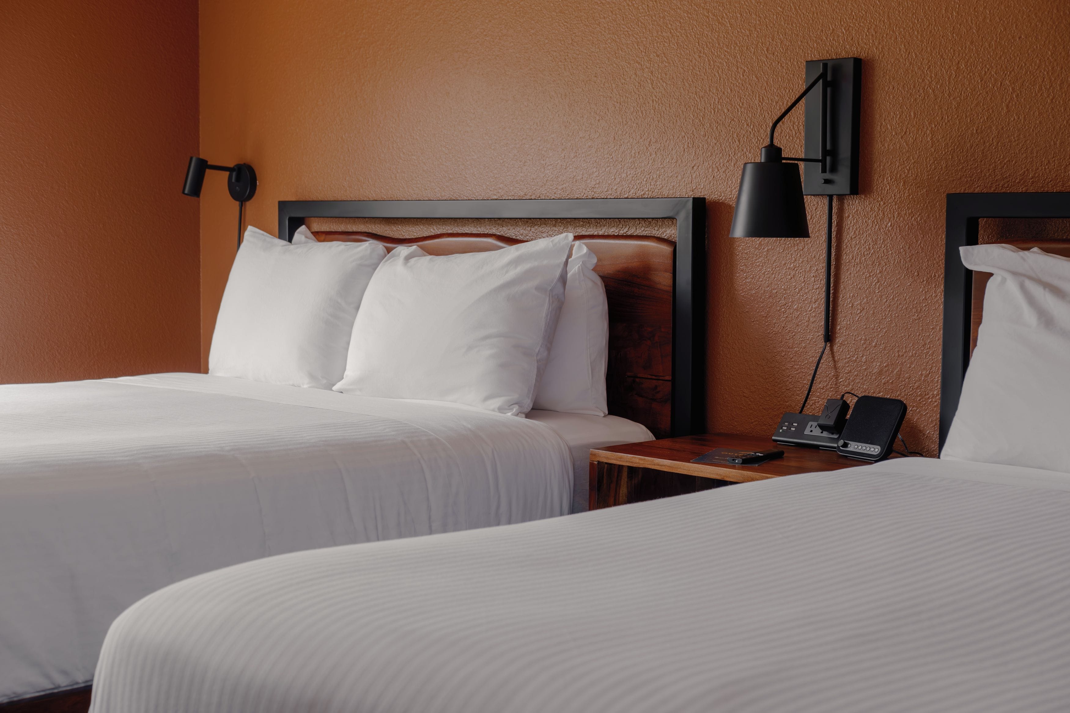 Une chambre d’hôtel avec deux lits, une table de chevet avec une lampe et un téléphone fixé au mur.