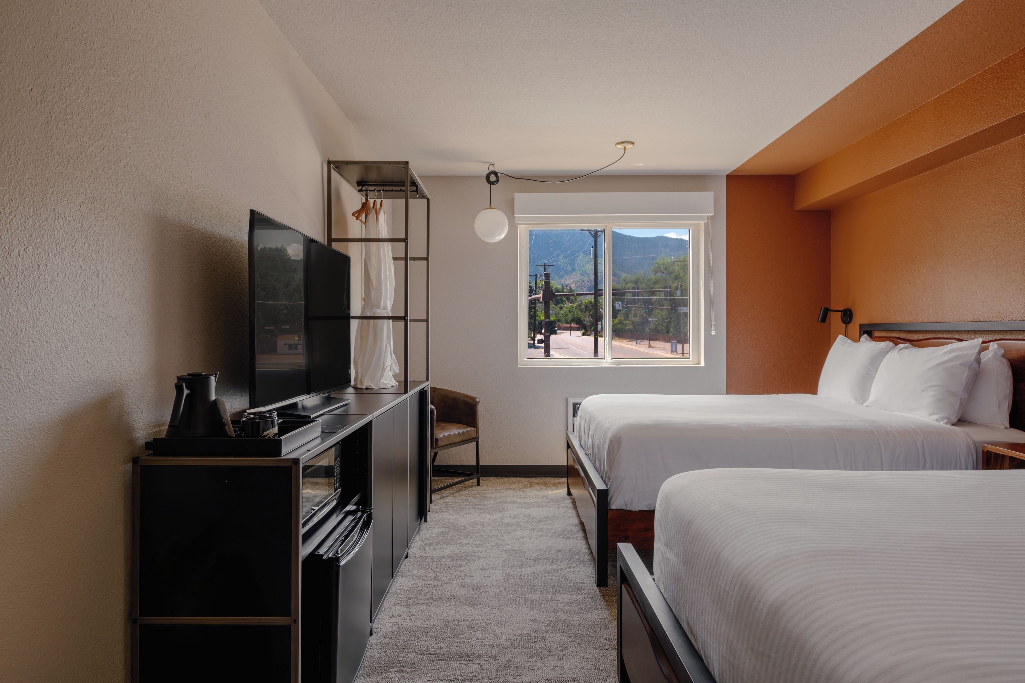 Habitación de hotel con cama, escritorio con televisor, silla y ventana con vistas a montañas.