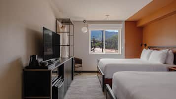 Habitación de hotel con cama, escritorio con televisor, silla y ventana con vistas a montañas.