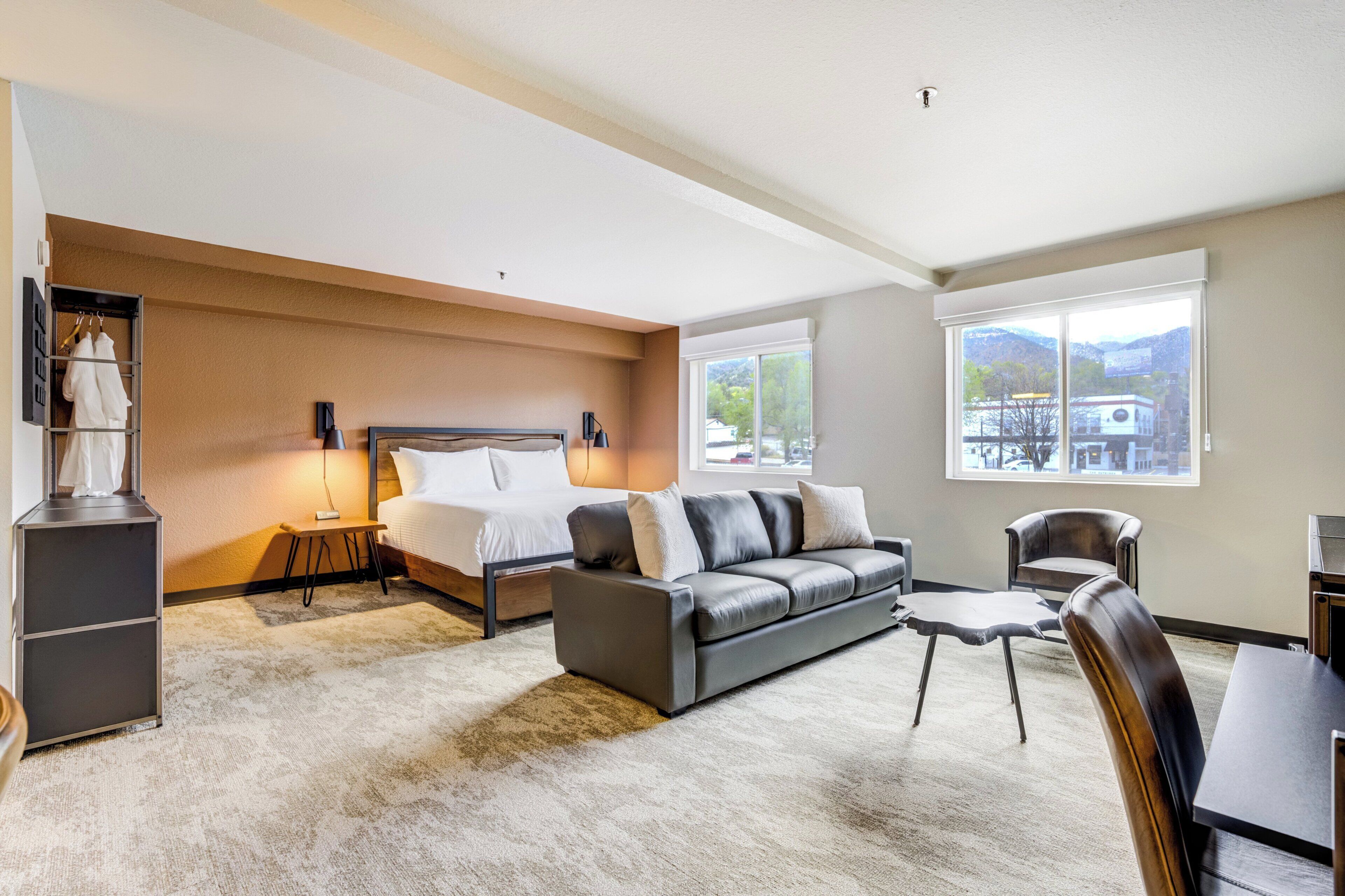 A modern hotel room with a bed, sofa, armchair, and a small table.