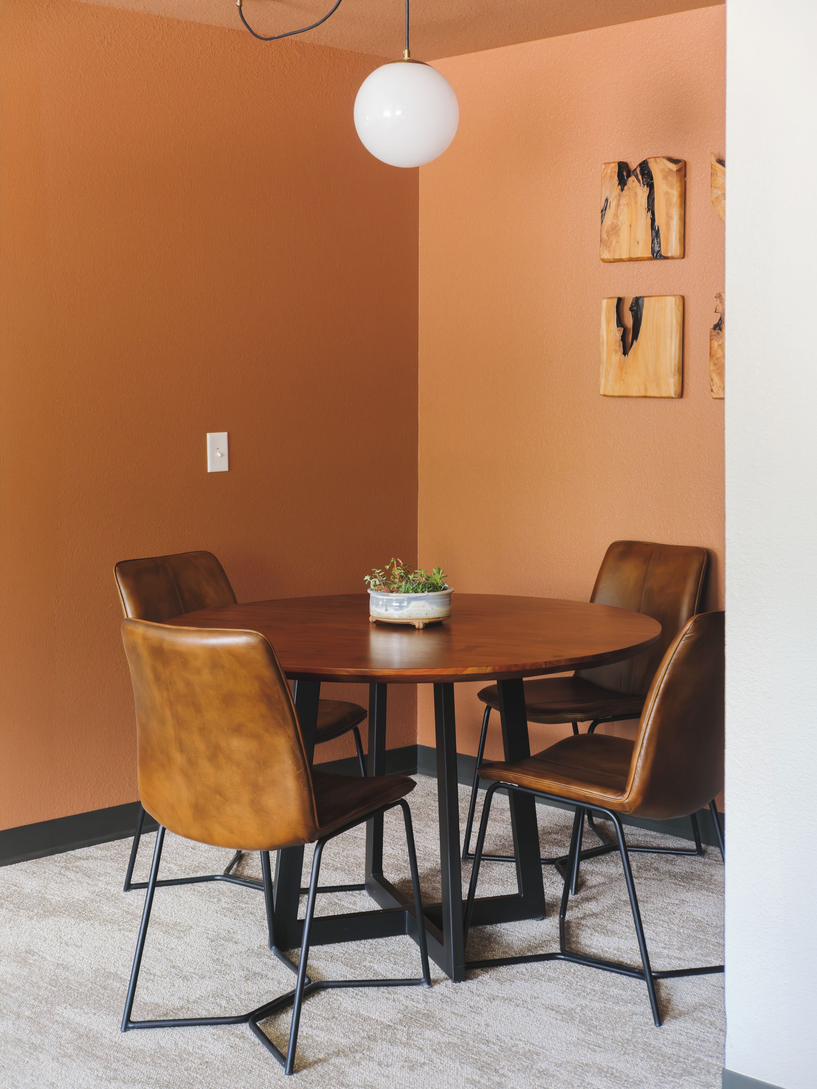 A conference room with a round table, four leather chairs, a potted plant, and a white pendant light.