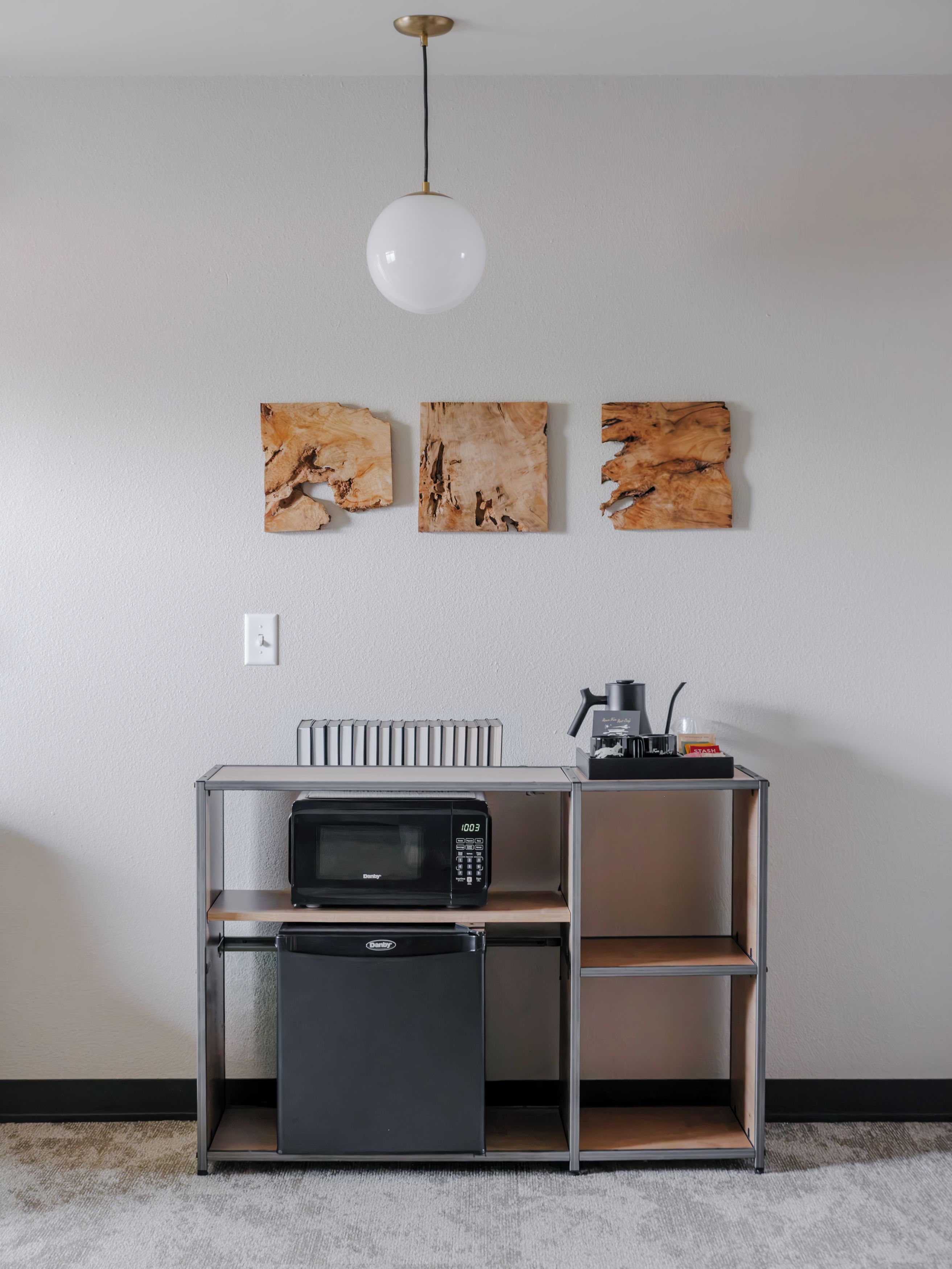 A kitchenette with a microwave, a small refrigerator, and a coffee maker on a metal shelf.
