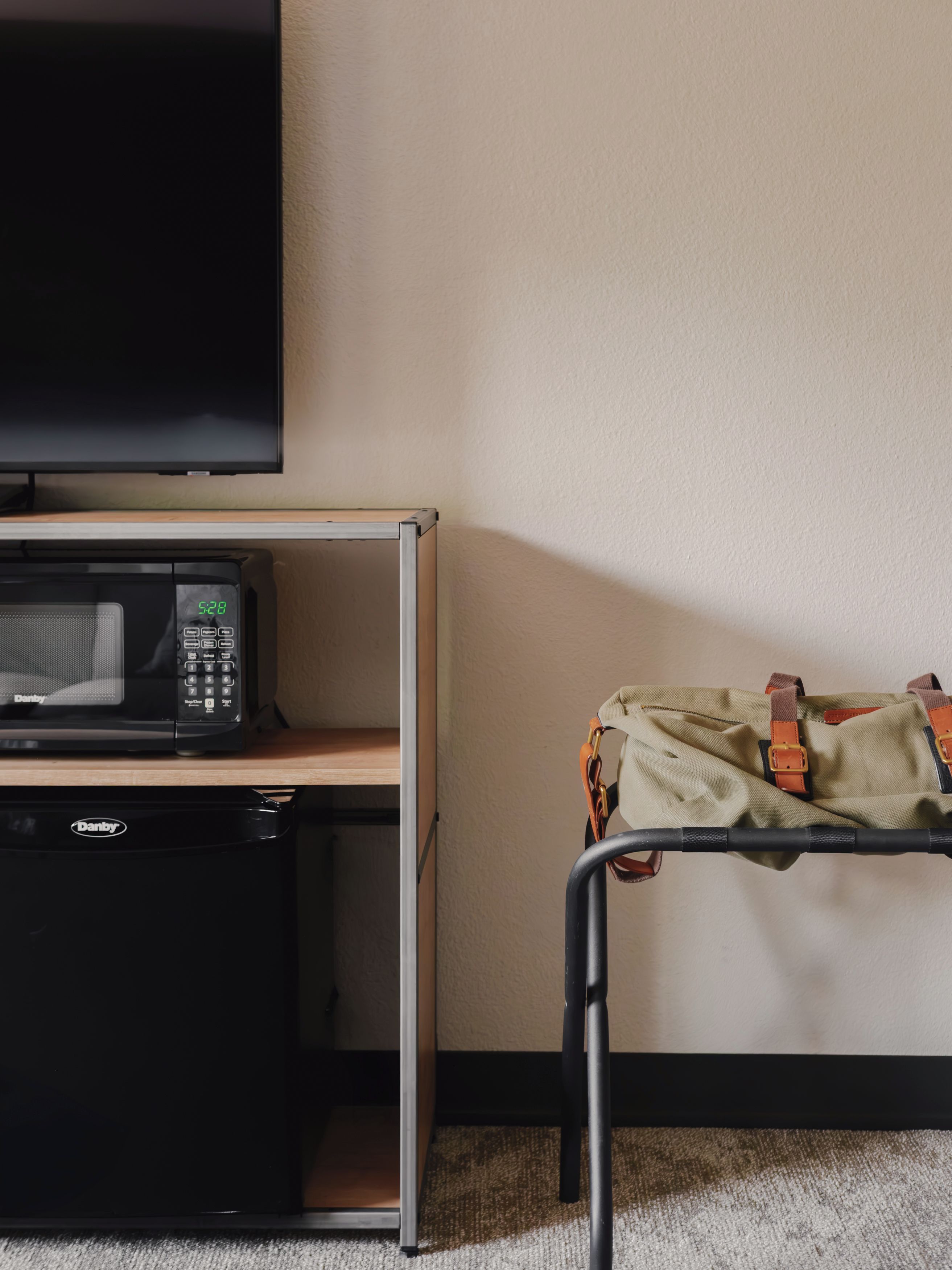 A room with a television mounted on the wall, a microwave, and a small refrigerator on a shelf.