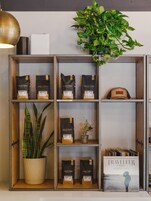 Interior de una cafetería con estantes que exhiben sacos de café, una planta en maceta y un libro titulado 'Traveller' de Chris Stapleton.
