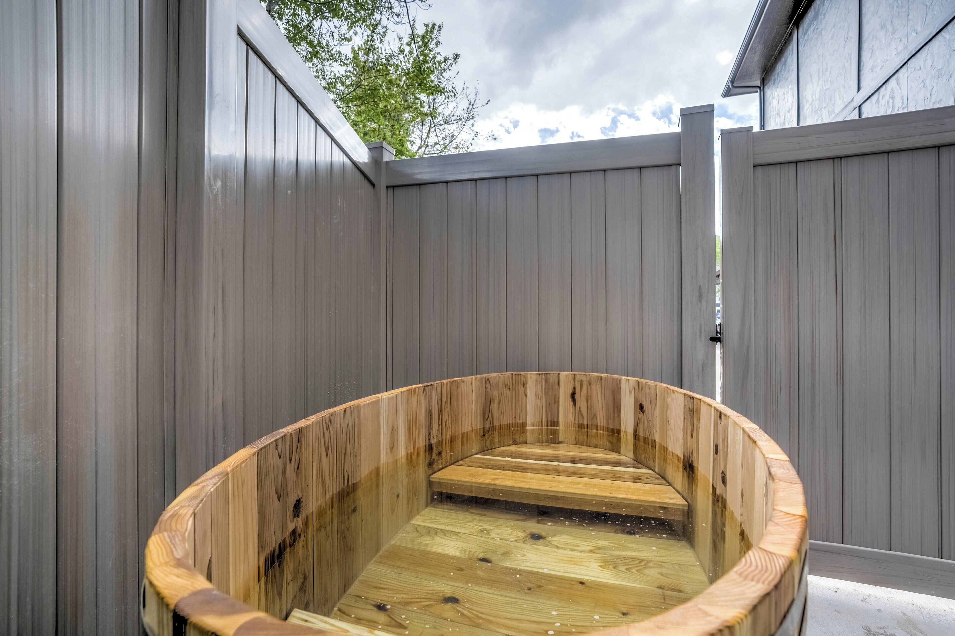 Een houten jacuzzi in een omheind buitengebied.