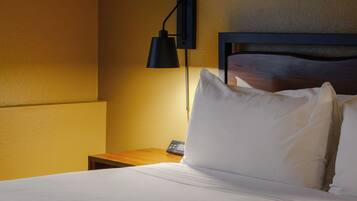 A hotel room with a neatly made bed, a bedside table, a lamp, and a wall-mounted light fixture.