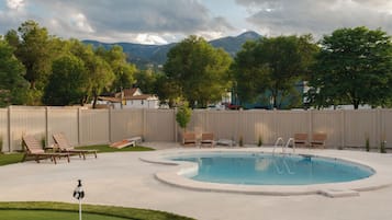 A swimming pool with a surrounding deck, lounge chairs, and a putting green.