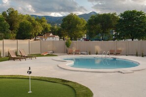 A swimming pool with a surrounding deck, lounge chairs, and a putting green. - The Outrider Hotel (Manitou Springs)