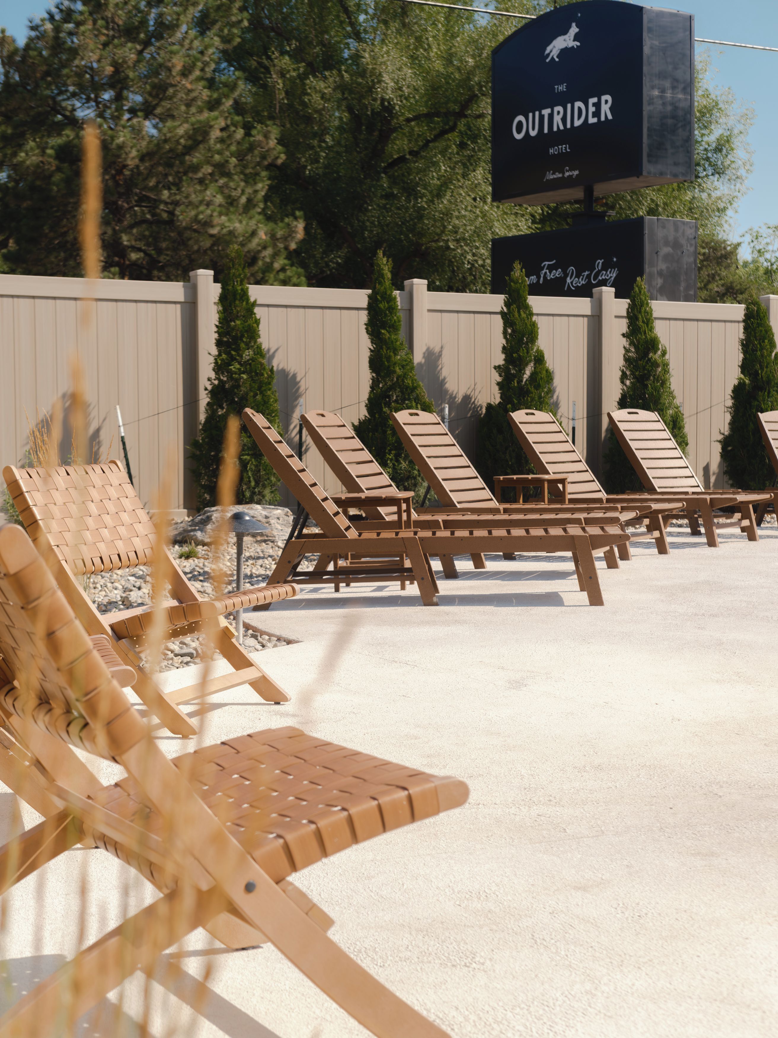 A row of wooden lounge chairs with a sign for 'The Outrider Hotel' in the background.