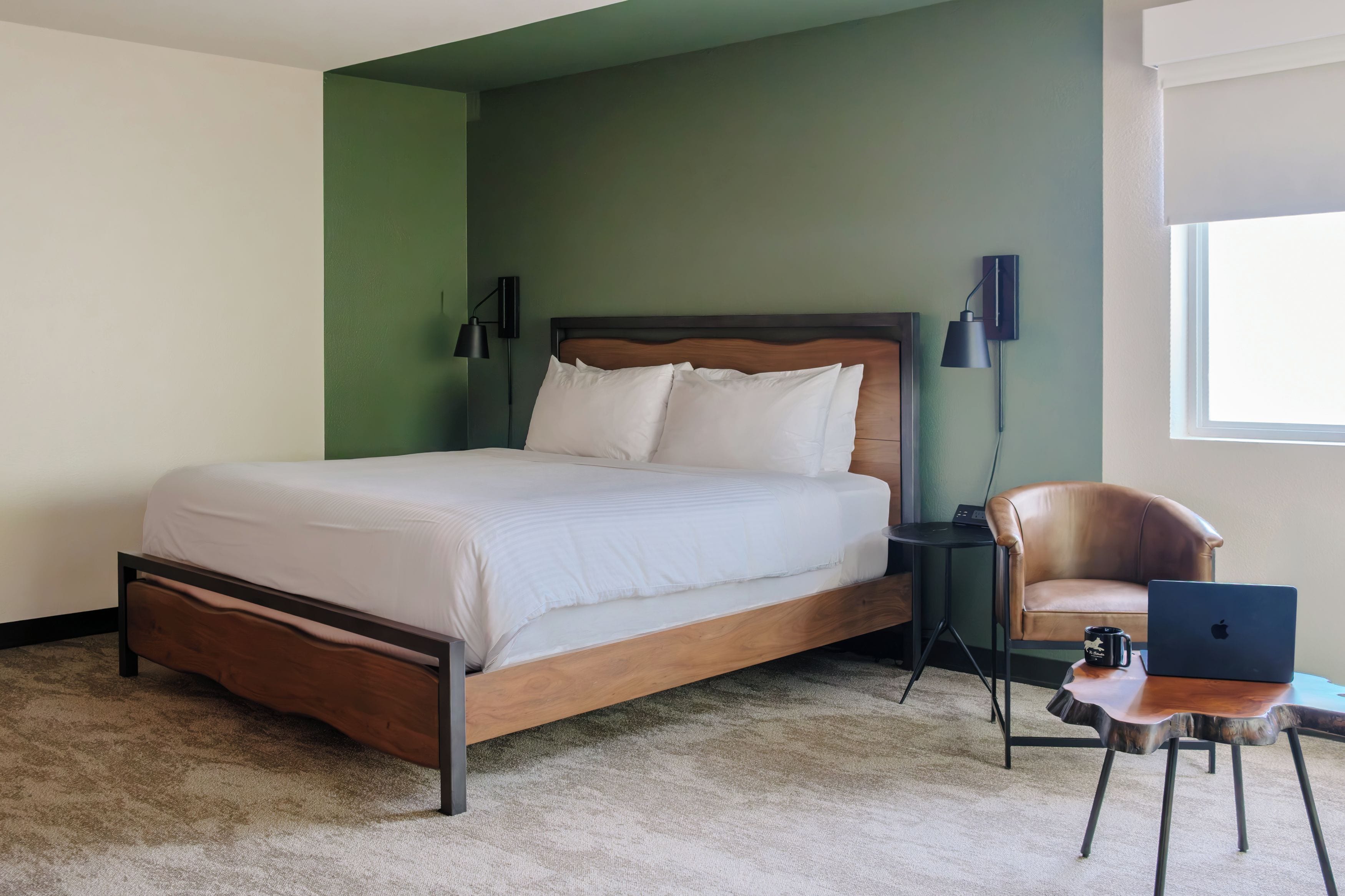 Un dormitorio con una cama de madera, una silla, un escritorio con una computadora portátil y una lámpara.