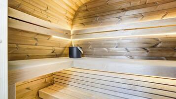 Un sauna aux murs et aux bancs en bois, avec un appareil de chauffage noir et une bande lumineuse le long du plafond.