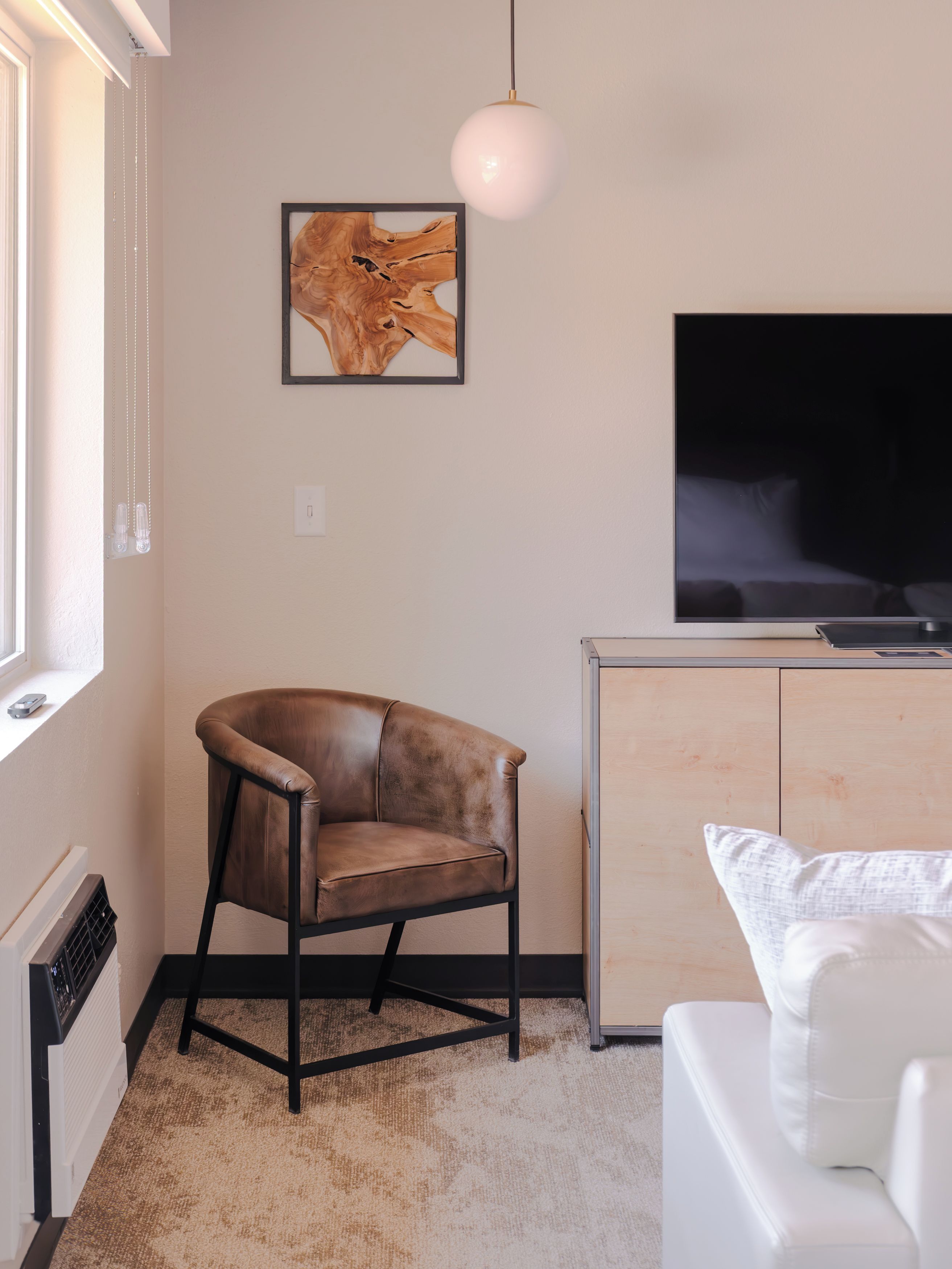 Uma sala de estar moderna com uma poltrona de couro, um sofá branco, uma TV de tela plana, um armário de madeira e uma obra de arte emoldurada na parede.