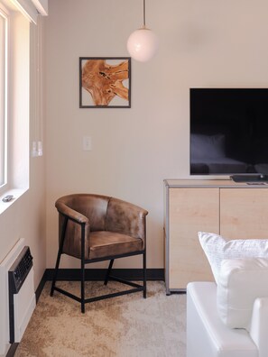 A modern living room with a leather armchair, a white sofa, a flat-screen TV, a wooden cabinet, and a framed artwork on the wall. - The Outrider Hotel (Manitou Springs)