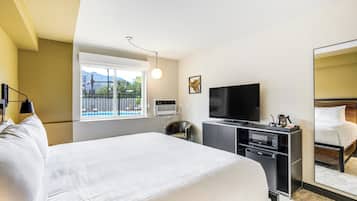 A hotel room with a bed, a TV, a desk with a microwave, and a view of a pool through a window.