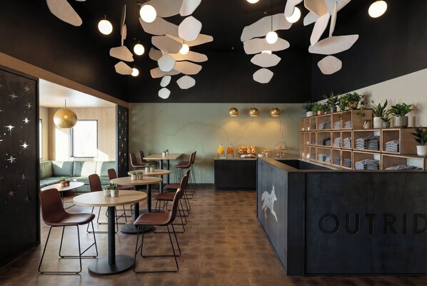 A modern interior with round tables and chairs, a reception desk, and a wall with a horse silhouette. - The Outrider Hotel (Manitou Springs)