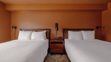 A hotel room with two beds, a nightstand, and a lamp between them.