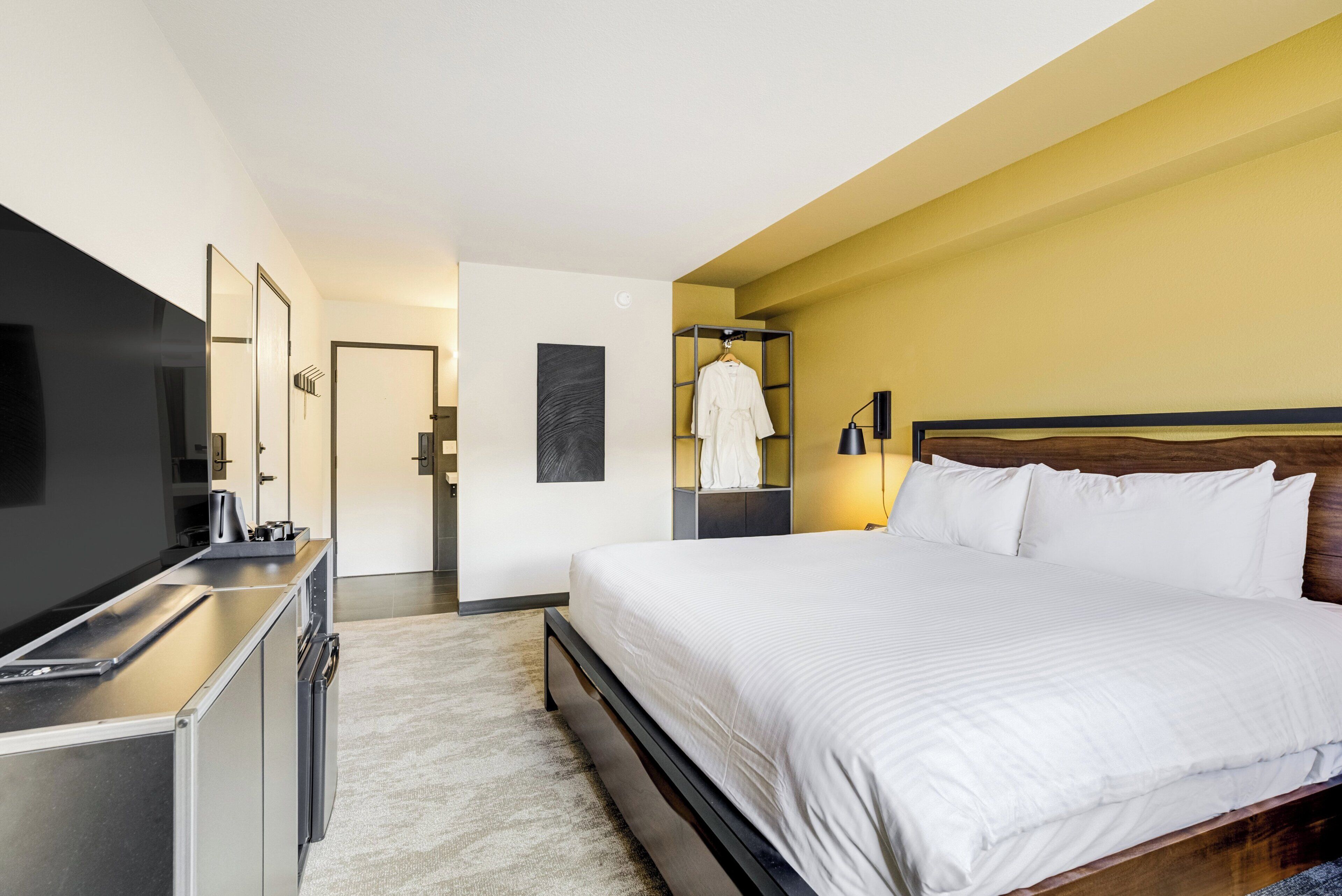 Una habitación de hotel moderna con una cama, un escritorio, un televisor y un armario.