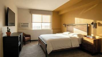 A bedroom with a bed, bedside table, lamp, TV, and a window.
