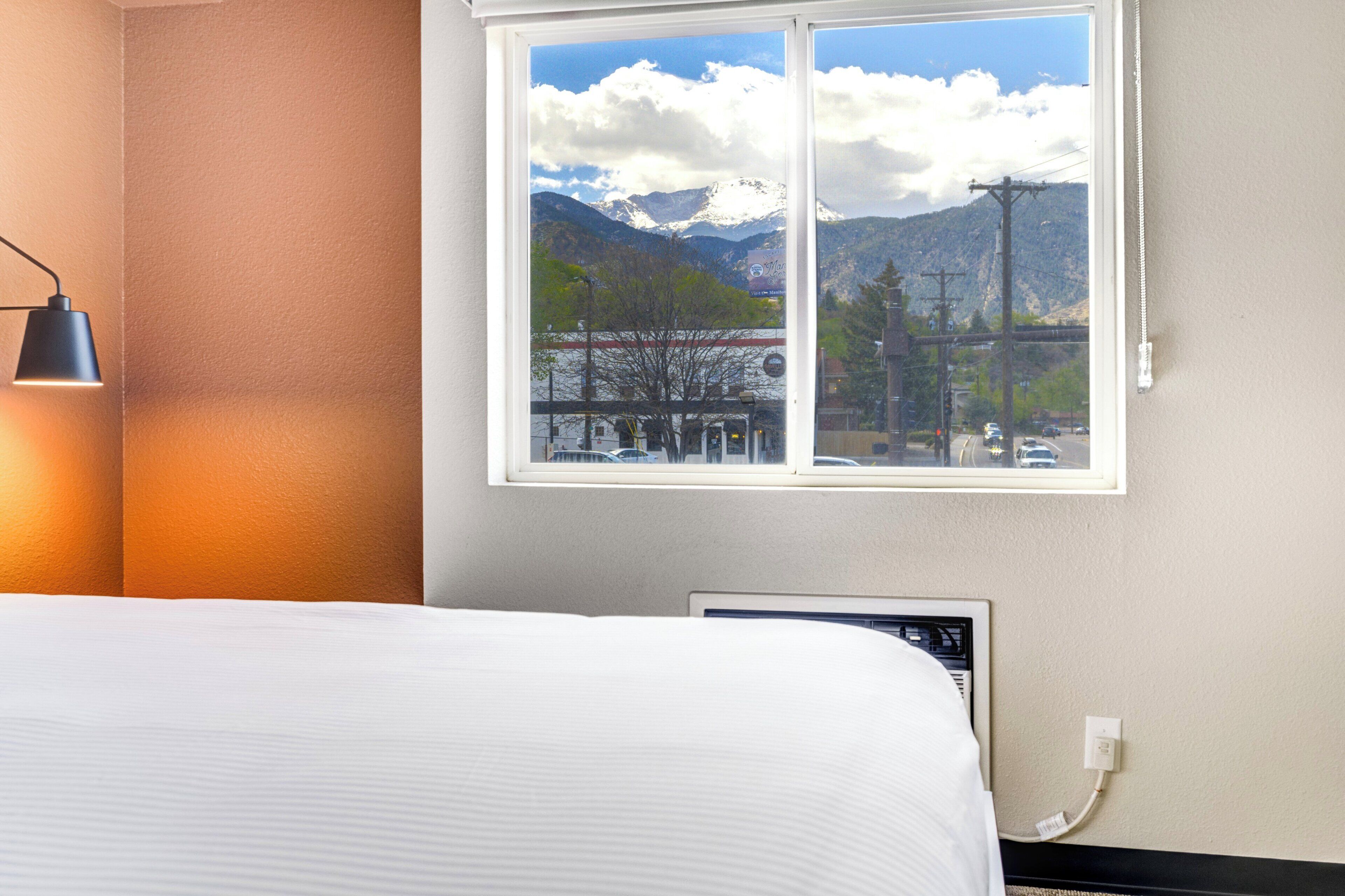 Habitación de hotel con cama, lámpara de noche, ventana con vista a la montaña y televisor montado en la pared.