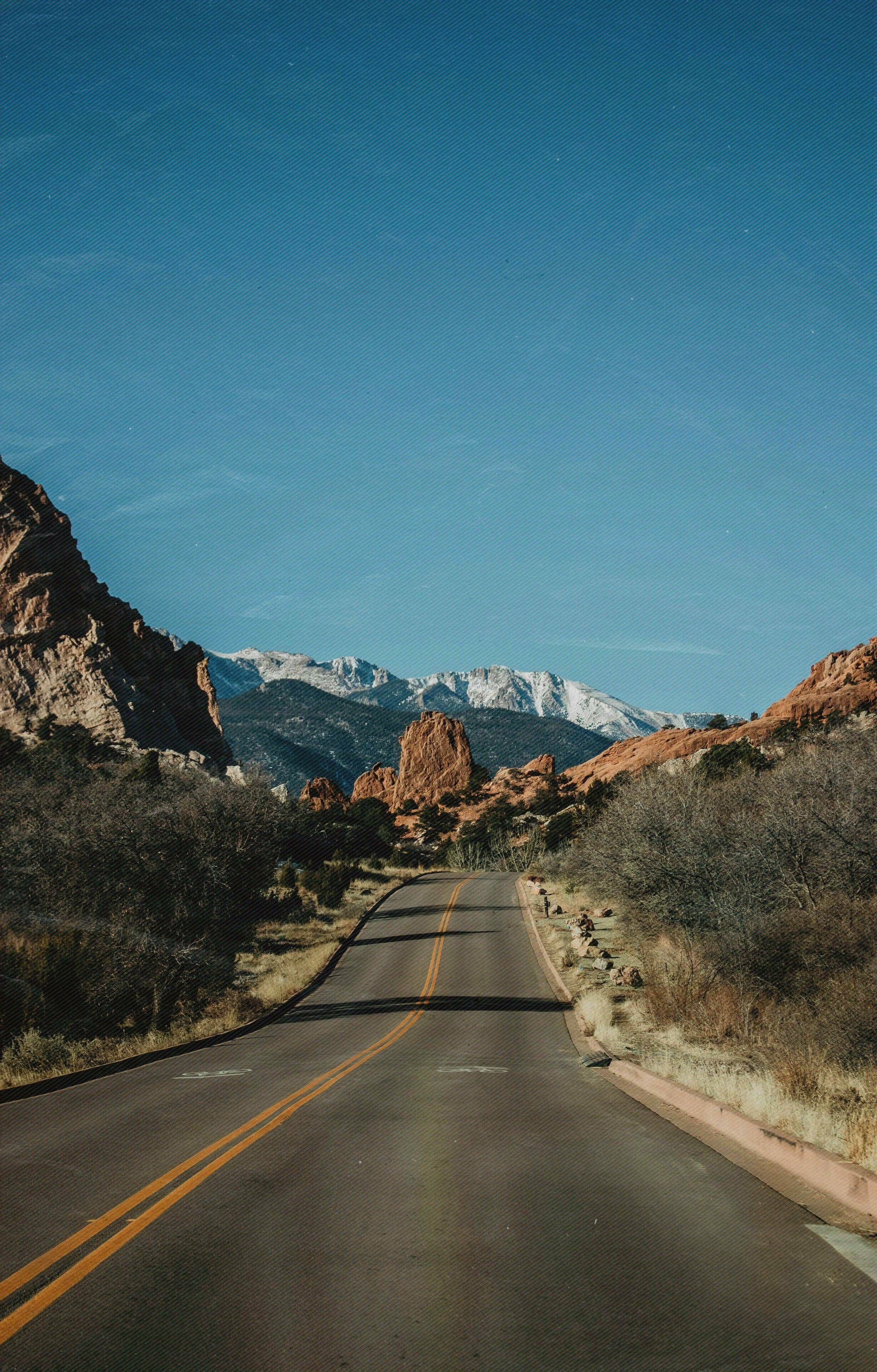 A road with a double yellow line, surrounded by rocky terrain and sparse vegetation.