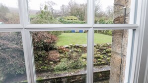 Una ventana con vista a un jardín que incluye un muro de piedra, césped y árboles.