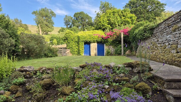 Un jardín con muro de piedra, puerta azul y césped.