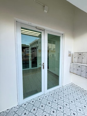 A room with a sliding glass door leading to a balcony, a tiled floor, and a wall-mounted electrical panel. - Sunny Beachy 2BR Spacious, Secure + Free Parking (San Juan)