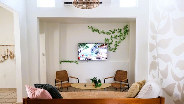 Una sala de estar acogedora con un sofá de madera, dos sillones de mimbre, una mesita redonda y un televisor montado en la pared.