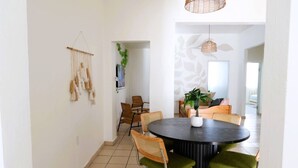 Un comedor con una mesa redonda, sillas tapizadas en verde y una lámpara de techo de fibras naturales.