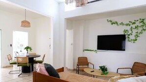 Una sala de estar moderna con un sofá, sillas, una mesa de comedor y un televisor montado en la pared.