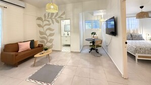 Een moderne woonkamer met een bank, salontafel en televisie. Er is een eethoek met een tafel en stoelen, plus een slaapkamer met een bed.