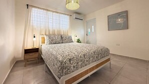 Een slaapkamer met een bed, nachtkastje, lamp, hanglamp, raam met gordijnen, airconditioning en een lijst met een foto aan de muur.