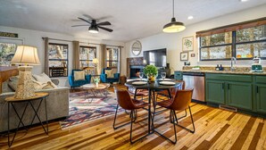 A spacious living area with a fireplace, a dining table with chairs, and a kitchen with green cabinets and a large window. - Locklyn`s Loft | Views, Hot Tub, Game Room & MORE! (Gatlinburg)