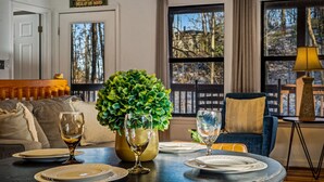A dining area with a table set for two, a potted plant, and a view of the outdoors through large windows. - Locklyn`s Loft | Views, Hot Tub, Game Room & MORE! (Gatlinburg)