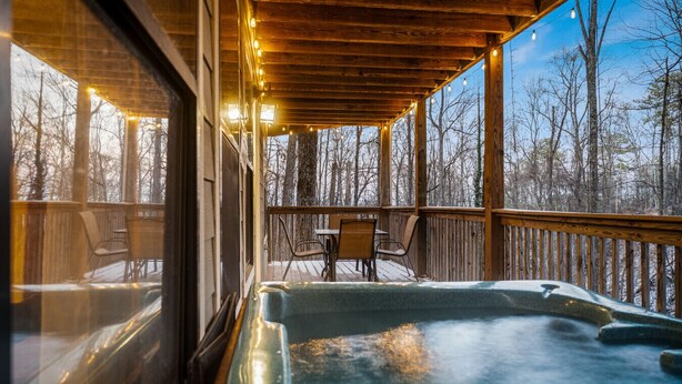 A wooden deck with a hot tub, chairs, and a table, overlooking a forested area. - Locklyn`s Loft | Views, Hot Tub, Game Room & MORE! (Gatlinburg)