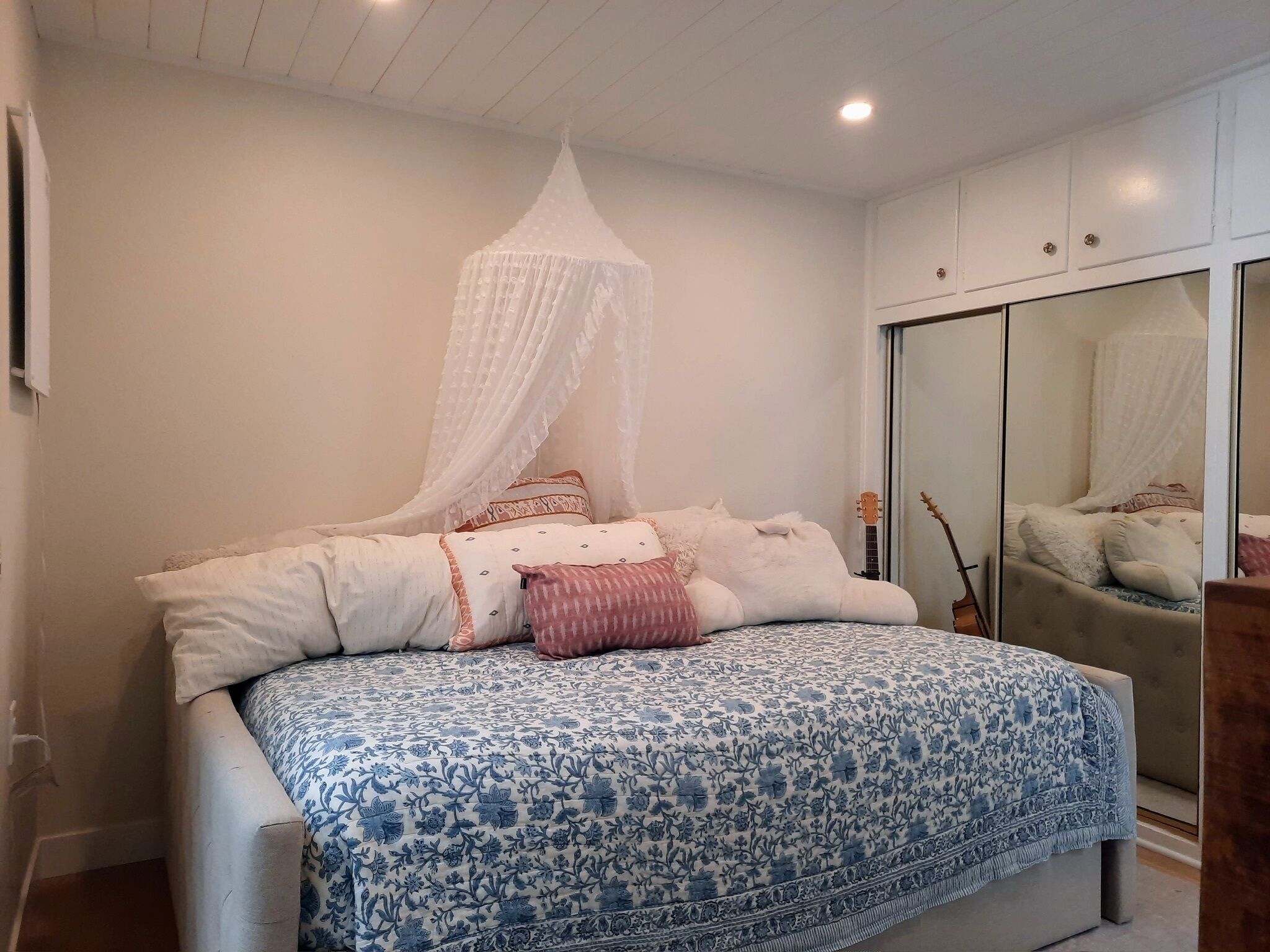 Een slaapkamer met een bed, witte muren, een plafondventilator en een kledingkast.