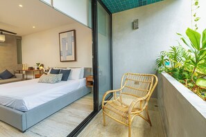 A modern bedroom with a large bed, a wicker chair, and a small table with books and a lamp. - Vibrante y Moderno Estudio Cerca de Quinta Avenida (Playa del Carmen)