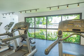 A gym with treadmills and elliptical machines, large windows with a view of greenery, and a ceiling with track lighting. - Vibrante y Moderno Estudio Cerca de Quinta Avenida (Playa del Carmen)