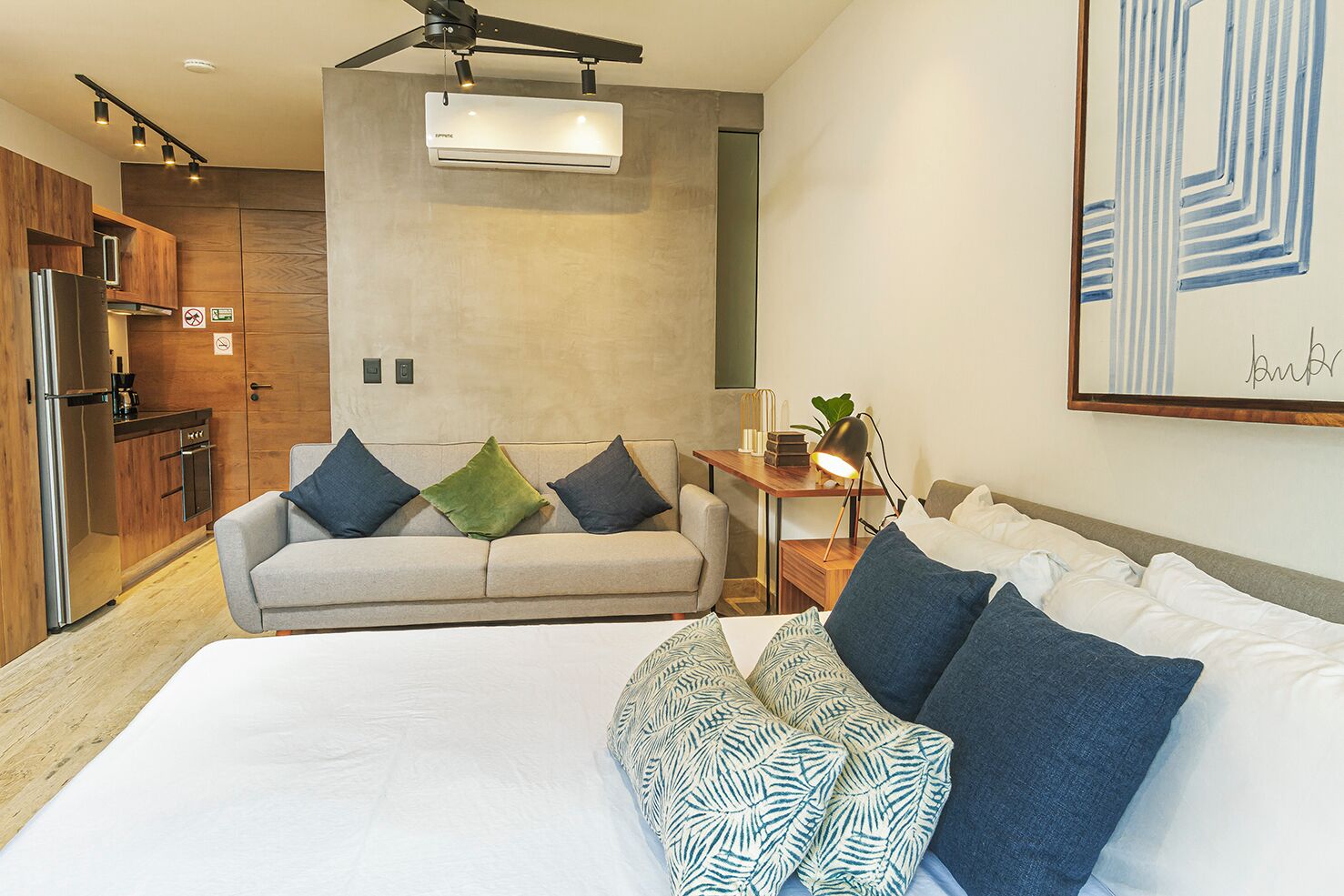 Een moderne hotelkamer met een bed, een bank, een bureau met lamp en een kitchenette.