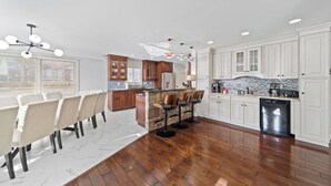 Una cocina moderna con armarios blancos, una isla central y un comedor con una mesa y sillas blancas.