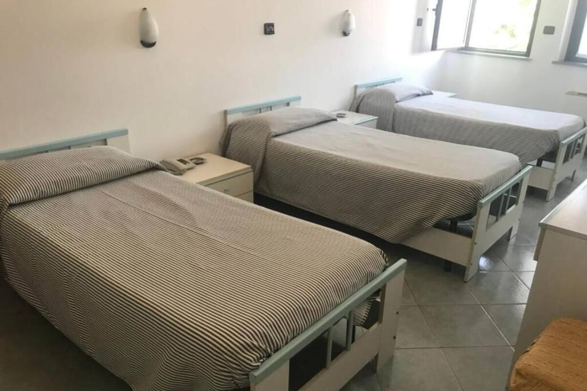 A room with three single beds, each with a striped bedspread and a nightstand.