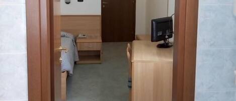 Una habitación con cama, escritorio y computadora. Se ve una puerta al fondo.