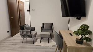 Ein modernes Wohnzimmer mit einem Flachbildfernseher, zwei grauen Sesseln, einem Holztisch und einem Bonsai-Baum.